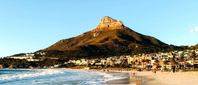Lion's Head rising above a seaside suburb and surf rolling onto a sandy beach