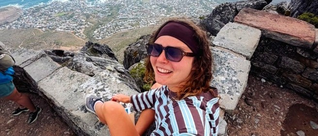 Traveller in sunglasses smiling on a clifftop ledge high above the city and coastline