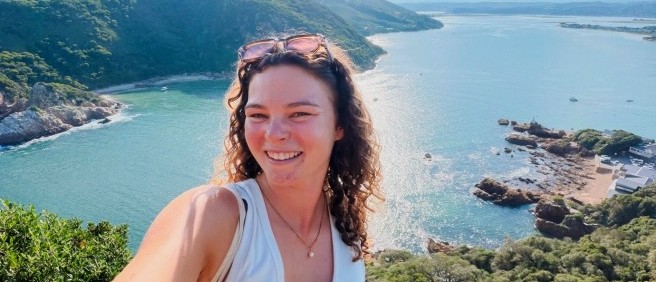 Traveller taking a selfie at a viewpoint above a calm blue inlet and rocky headland