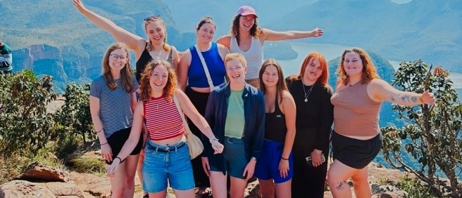 Group of travellers celebrating on a rocky viewpoint above a deep, forested canyon