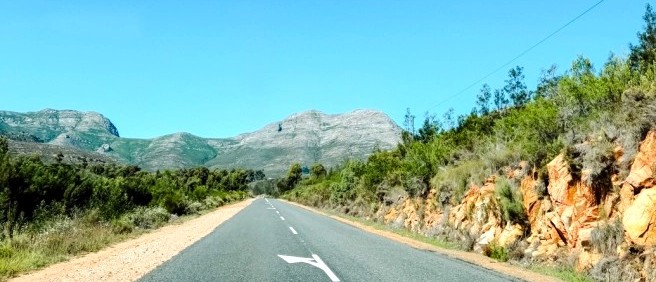 Empty mountain road running between green bush, rocky cuttings and distant peaks