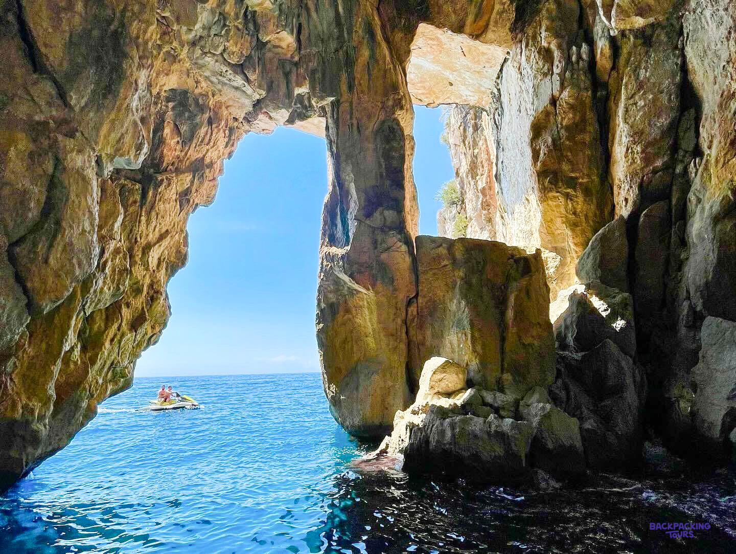 A boat passing a rock arch at the mouth of a sea cave on the coast near Himarë