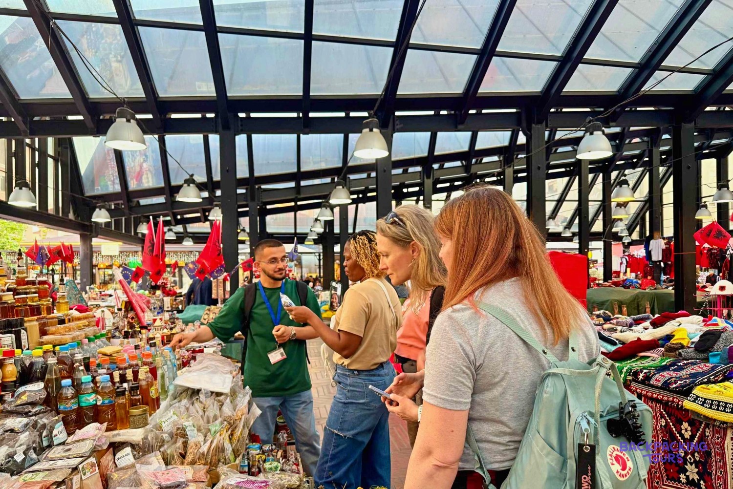A guide showing three travellers the stalls of Tirana's New Bazaar under its glass roof
