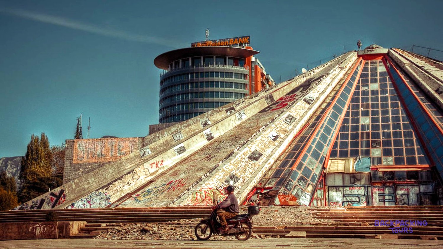 The Pyramid of Tirana covered in graffiti before its renovation, with a moped passing below