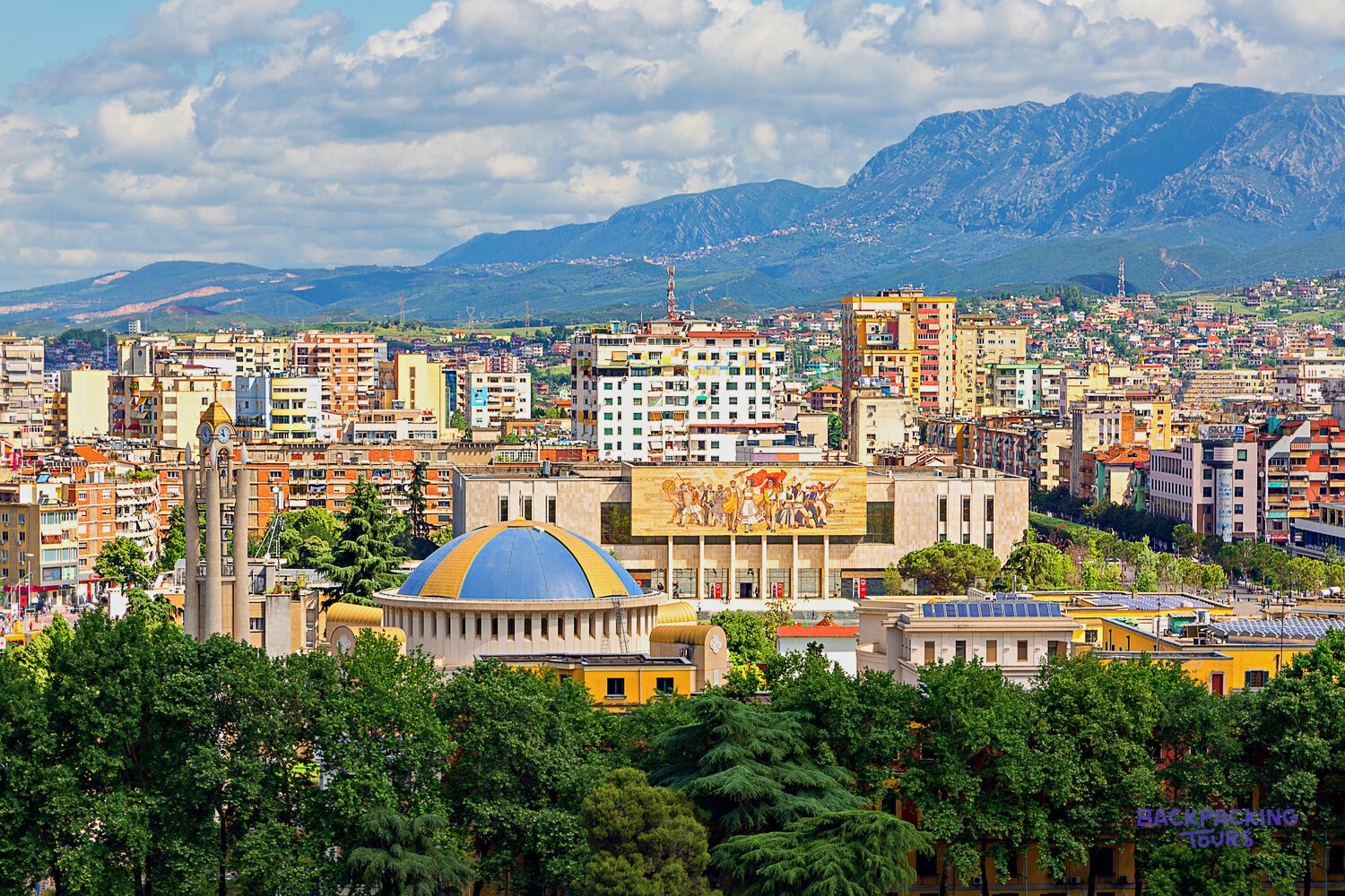 Tirana's rooftops and the mosaic facade of the National History Museum below the mountains