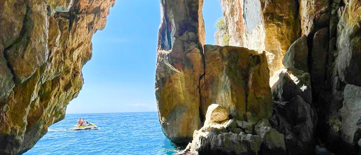 A boat passing a rock arch at the mouth of a sea cave on the coast near Himarë