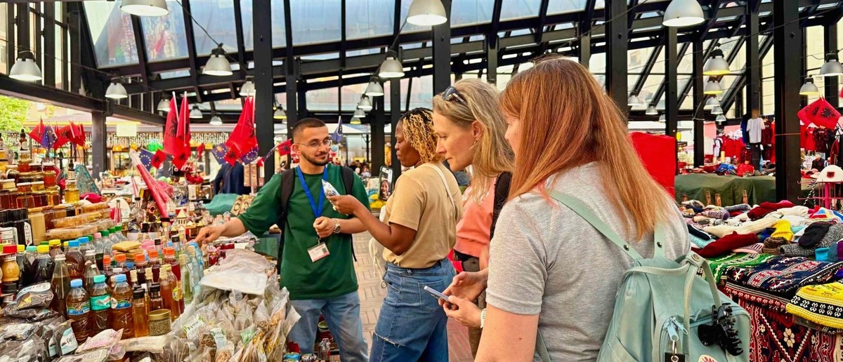 A guide showing three travellers the stalls of Tirana's New Bazaar under its glass roof