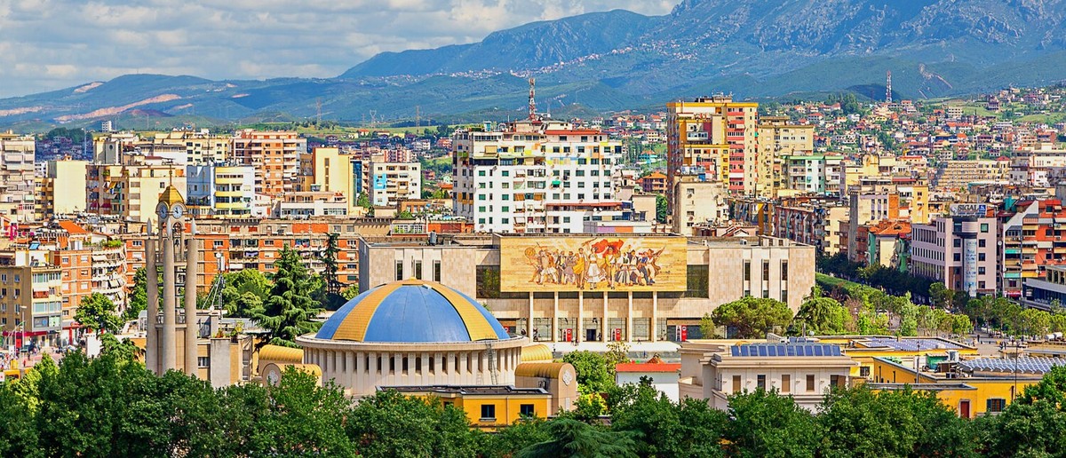 Tirana's rooftops and the mosaic facade of the National History Museum below the mountains