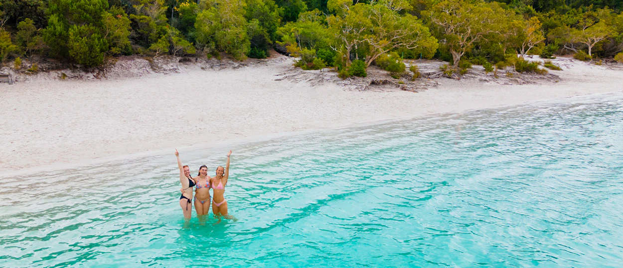 Three happy women with raised arms enjoy the clear turquoise water at Lake McKenzie, Fraser Island.