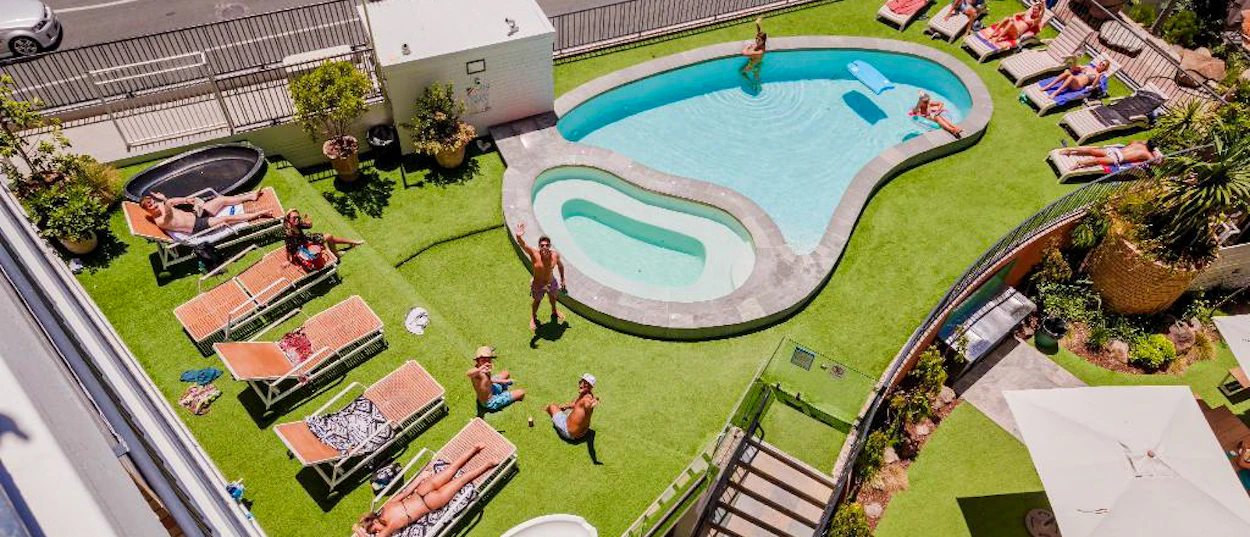 Backpackers relax by the pool, sunbathing on lounge chairs at a hostel in Surfers Paradise.