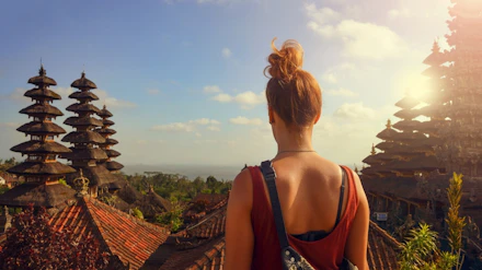 Woman with a bun admiring the intricate tiered roofs of a Balinese temple on a sunny day.
