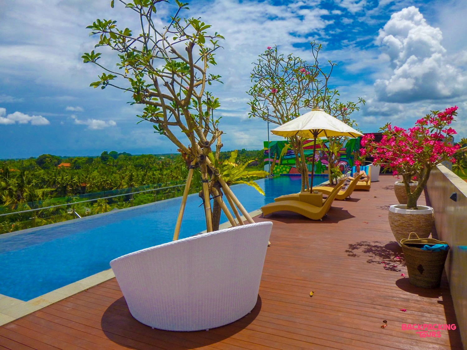 Relaxing infinity pool with lounge chairs and tropical plants, offering panoramic views of Ubud, Bali.
