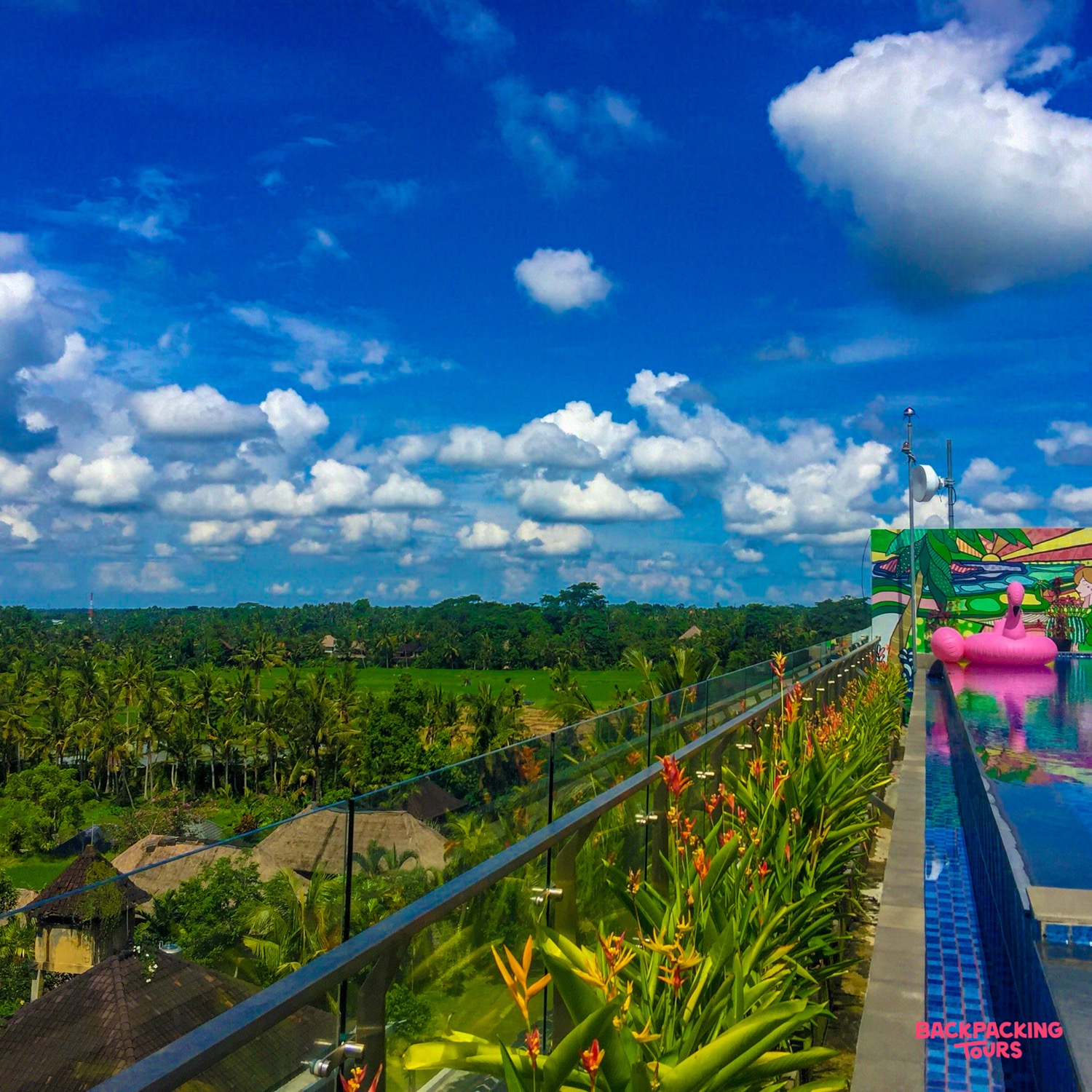 Rooftop infinity pool with a pink flamingo float, overlooking lush green rice fields in Ubud, Bali.