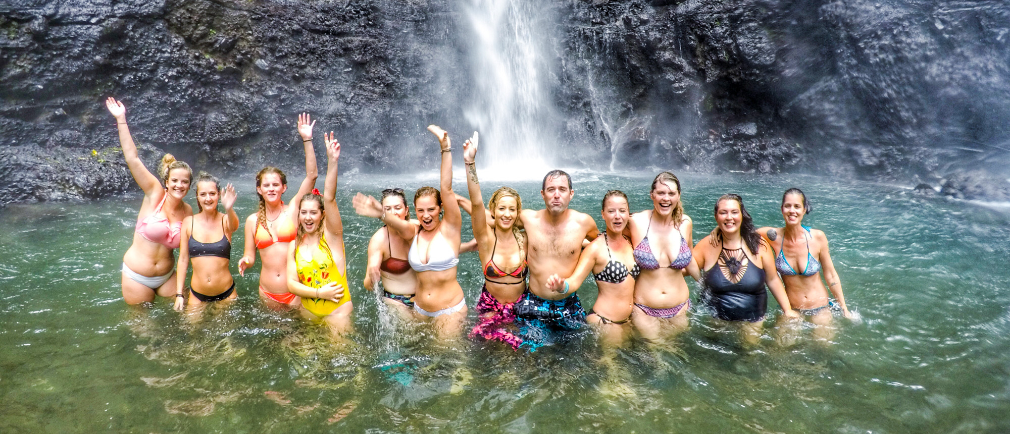 Backpacking group swimming and cheering at the base of Sekumpul Waterfall