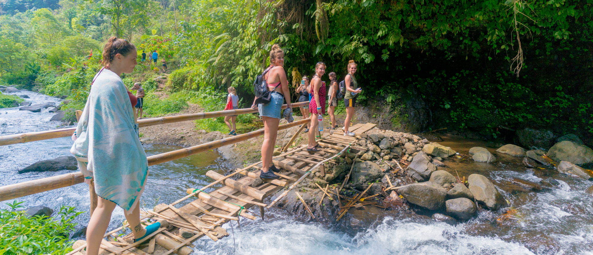 Travellers crossing a bamboo bridge over a jungle stream
