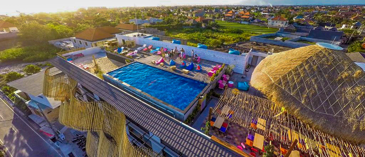 Vibrant rooftop pool and lounge area in Canggu with colorful bean bags under a golden sunset.