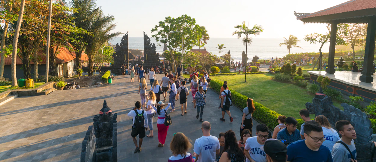 Many tourists walk through Tanah Lot temple complex towards the ocean at sunset in Bali.