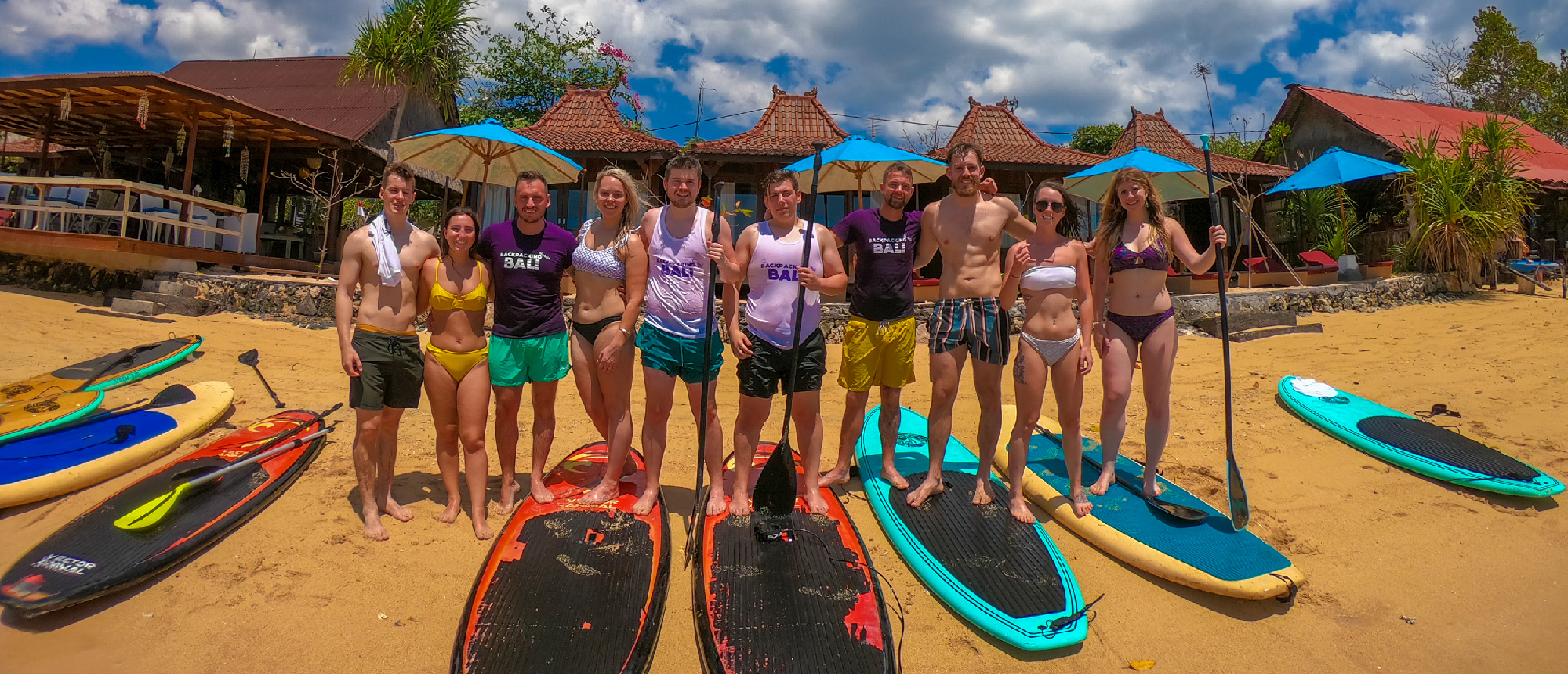 Backpacking group posing with paddleboards on the sandy beach in Nusa Lembongan