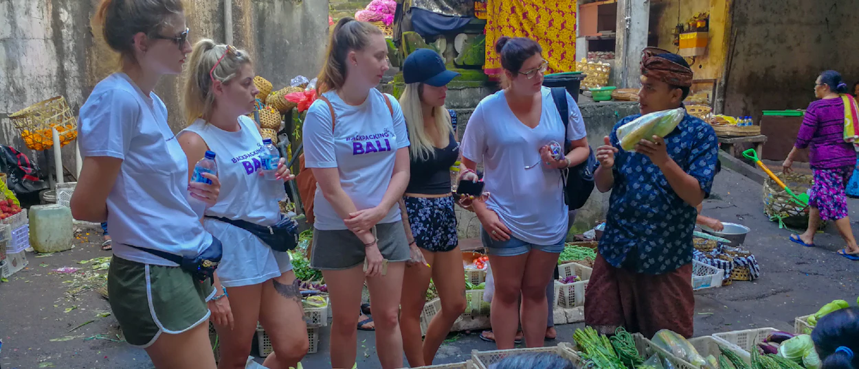 Tourists learning about local produce from a Balinese man at a vibrant market in Ubud.