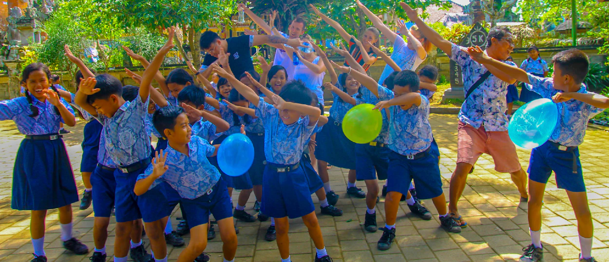 Happy students and backpackers dabbing together with balloons at a local school in Ubud, Bali.