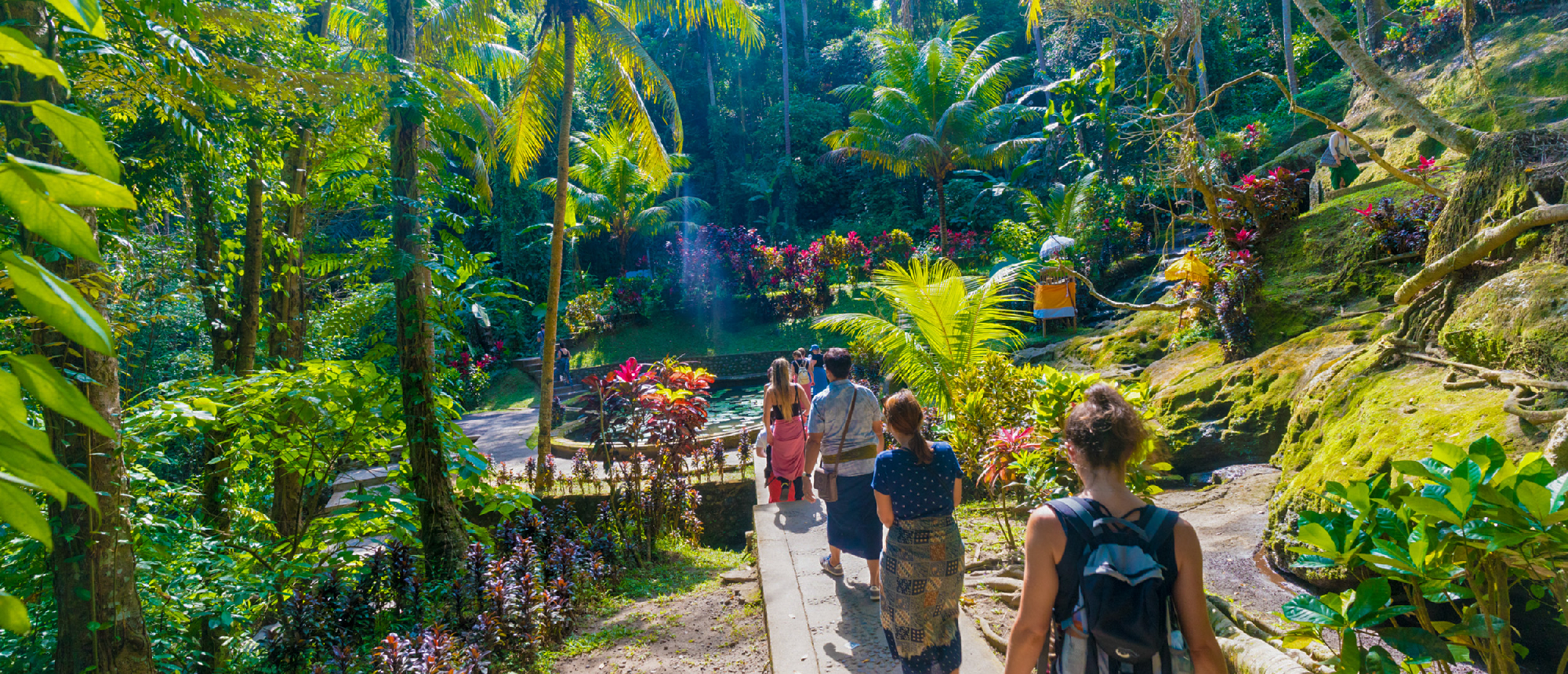 Backpacking group hiking down forest path toward waterfall near Ubud