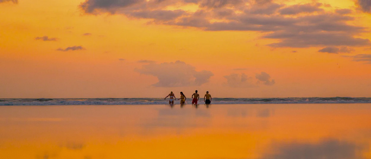 Four friends silhouetted against a vibrant orange sunset on the calm waters of Gili Trawangan.