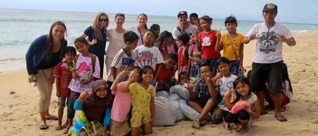 Smiling adults and children on a sandy Bali beach after an environmental education activity.