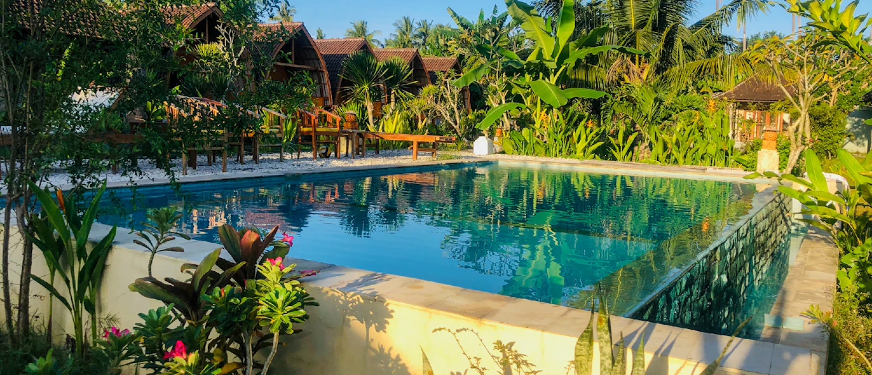 A serene swimming pool surrounded by lush tropical plants and traditional bungalows in Nusa Penida.