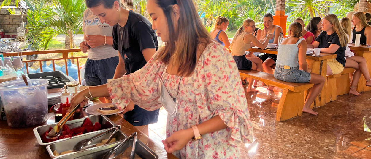 Young women serving themselves food and socializing at a casual outdoor dining area in Nusa Penida.
