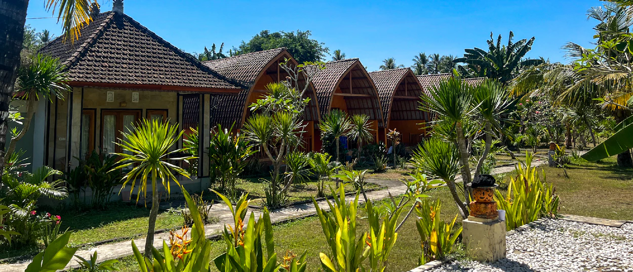 Sunny view of traditional and arched bungalows amidst green gardens and palm trees in Nusa Penida.