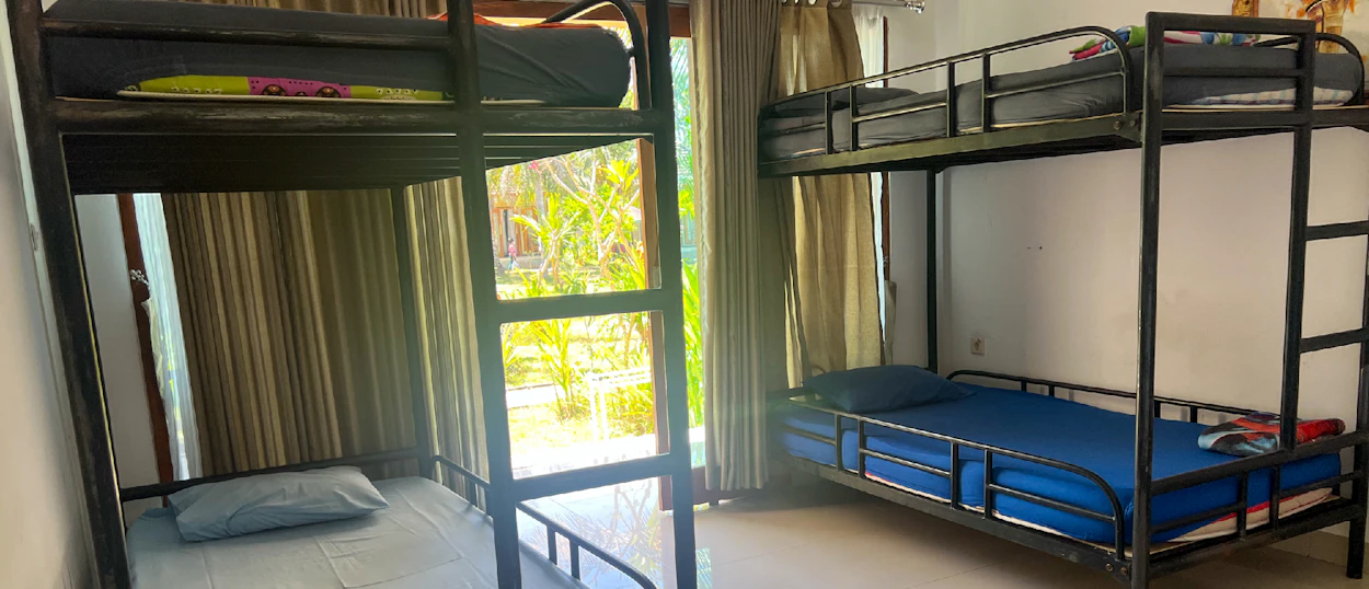 Two metal bunk beds with mattresses and pillows in a bright dormitory room on Nusa Penida.