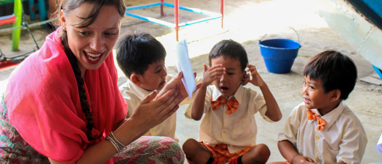 A joyful volunteer engages three young children sitting on the floor during a teaching session in Bali.