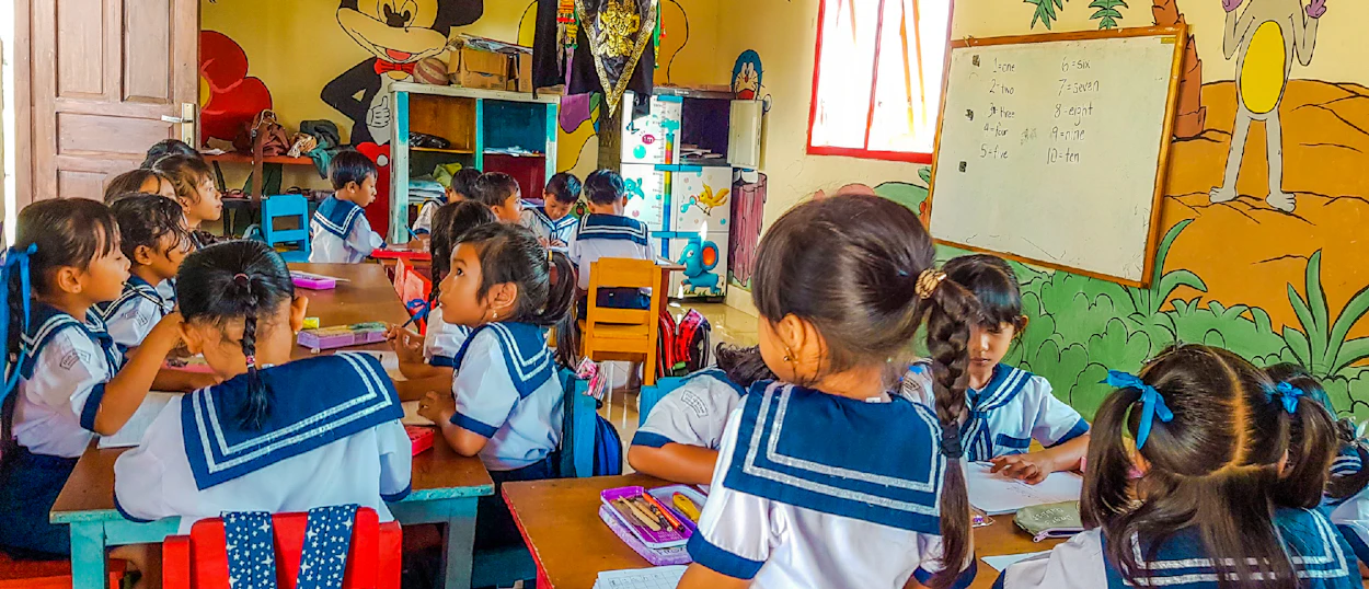 Young children in sailor-style uniforms sit at desks, engaged in learning within a colorful kindergarten classroom in Bali.