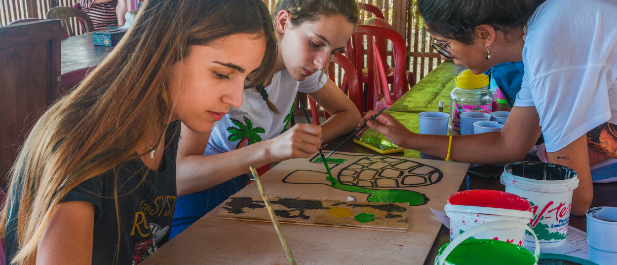 Three volunteers focused on painting green turtle designs on wooden boards in Nusa Penida, Bali.