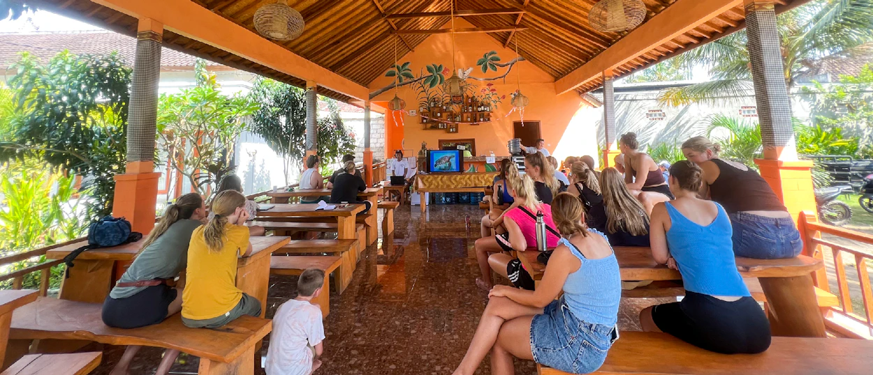 A group of young travelers listens attentively to an introduction in an open-air pavilion in Nusa Penida.