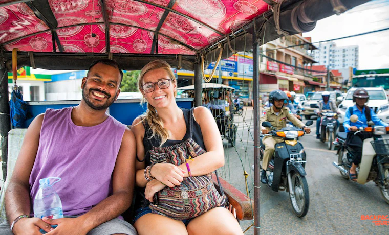 Two smiling travelers enjoying a tuk-tuk ride through the bustling streets of Phnom Penh.