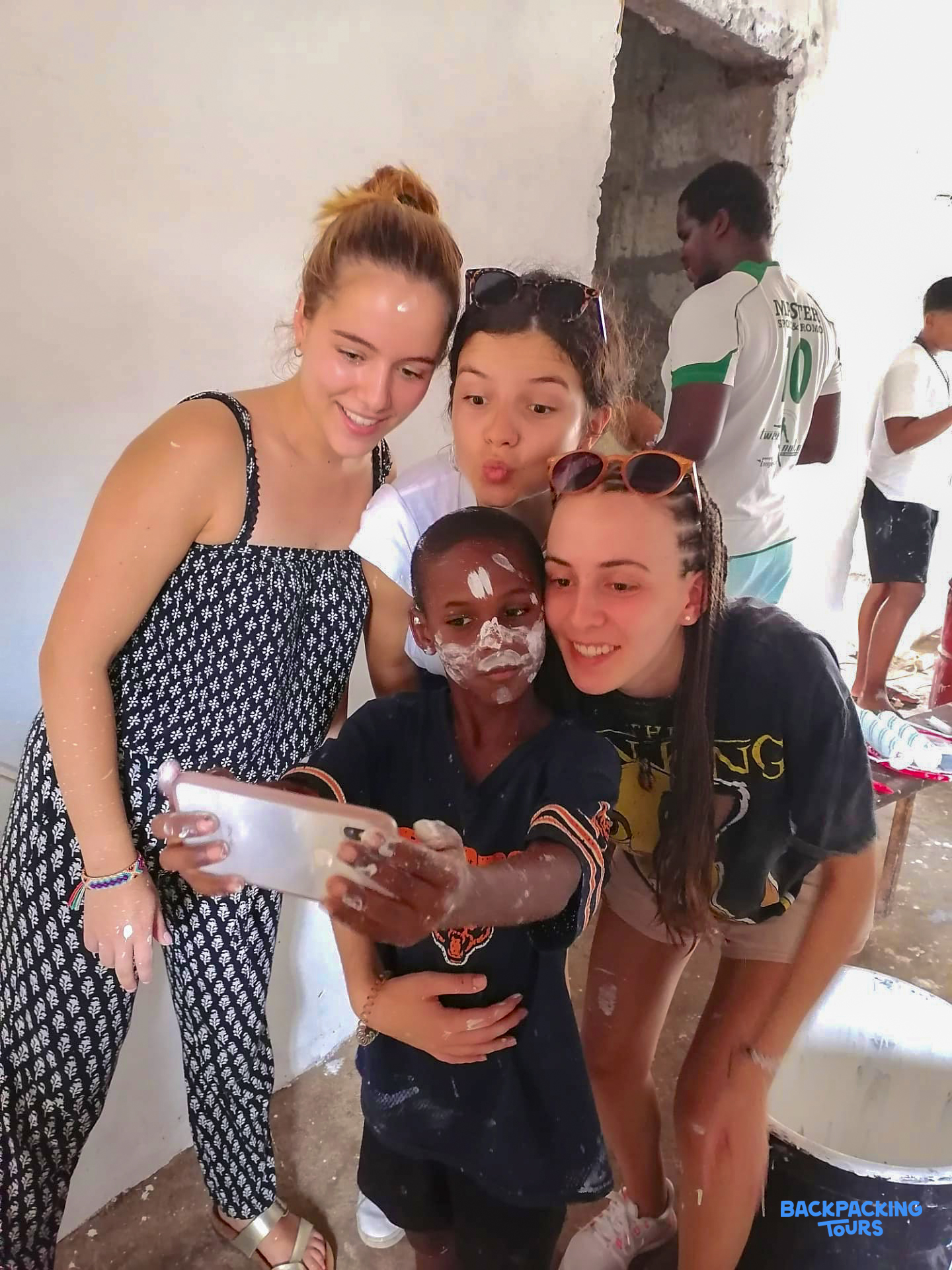 Volunteers and a local boy covered in paint playfully take a selfie during a construction project.