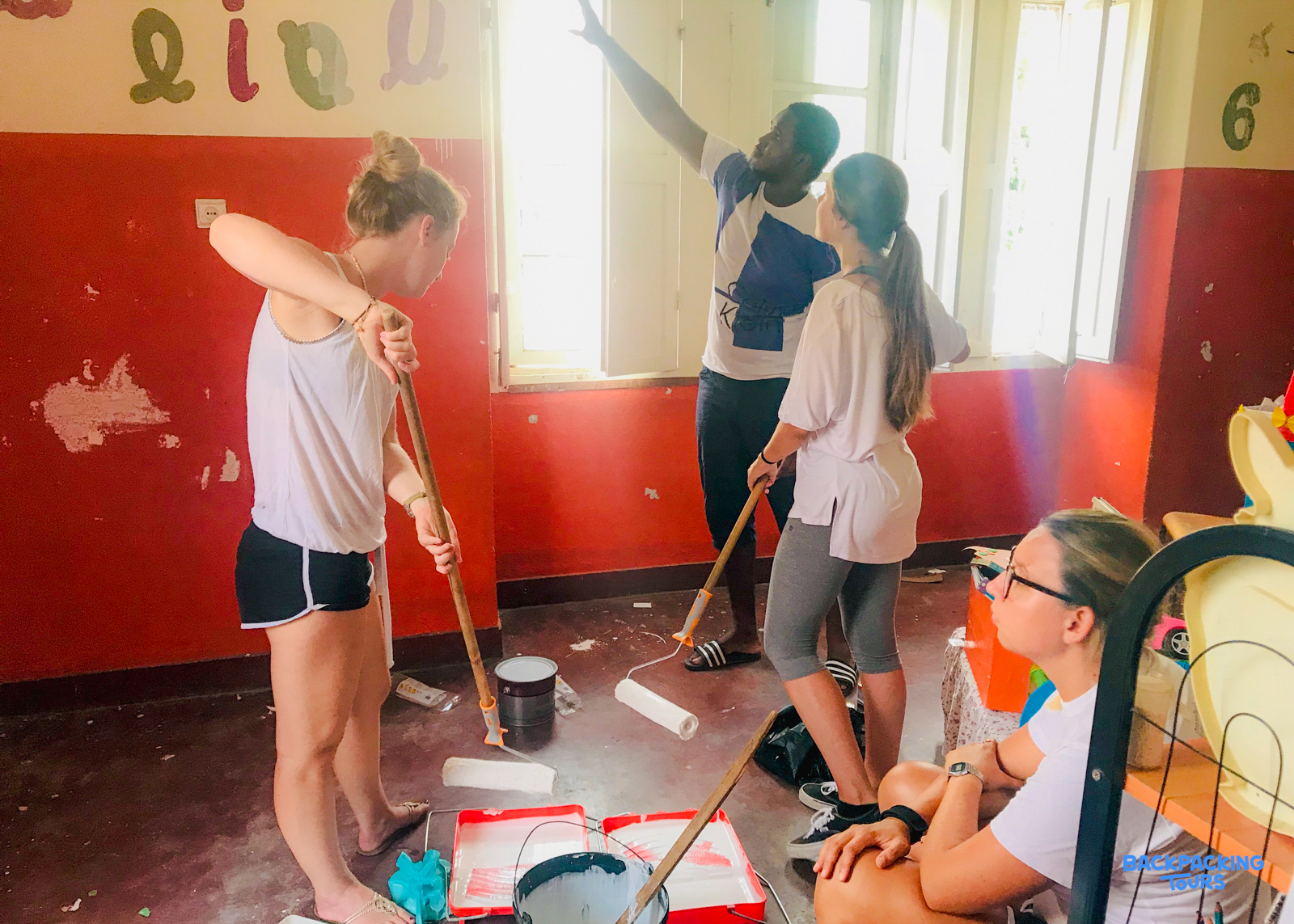 A group of volunteers actively paints a community room, transforming the red walls with fresh white paint.