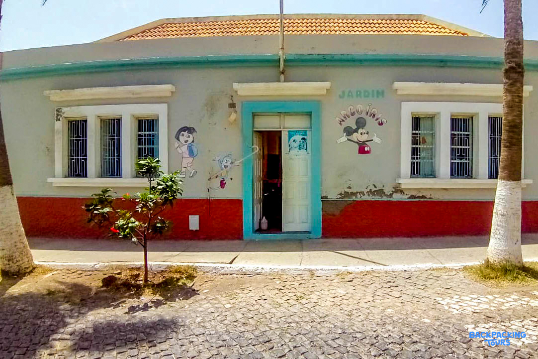 A colorful kindergarten building with cartoon murals and a bright blue door in Cape Verde.