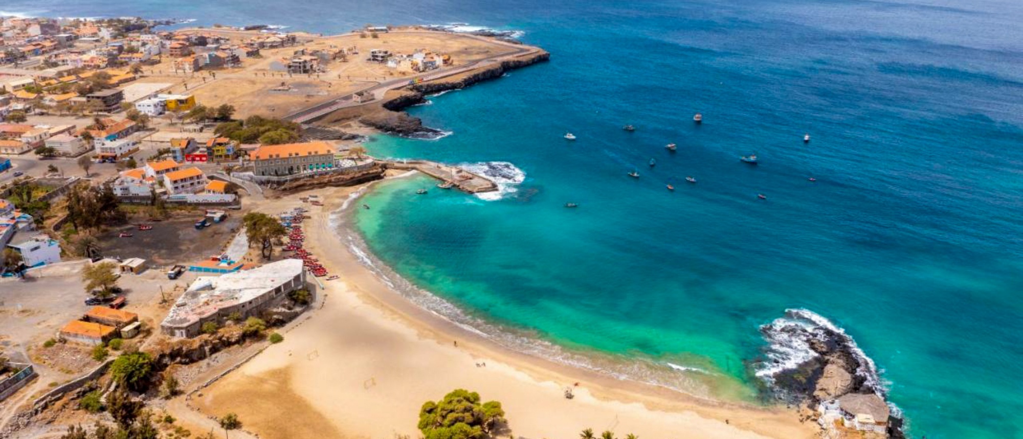 Beautiful aerial view of a coastal town, sandy beach, and clear blue-green ocean with boats.