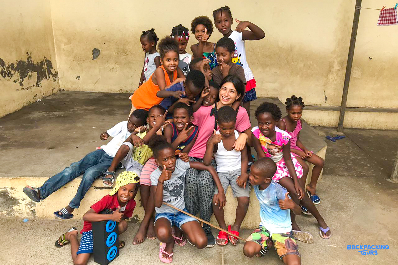 A volunteer teacher surrounded by a large group of smiling, playful children in Cape Verde.