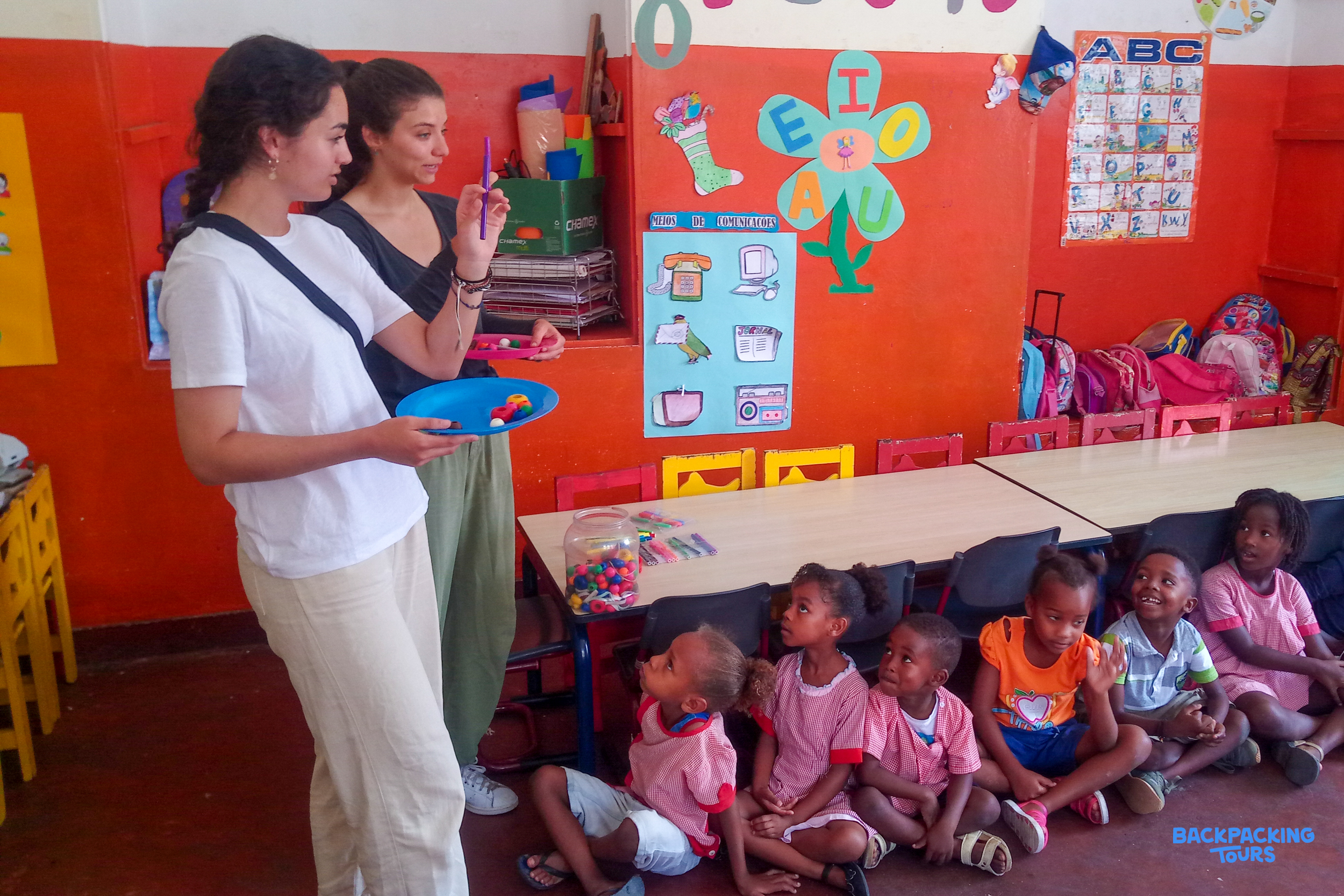 Volunteers engage with young children during a lesson in a vibrant classroom setting.