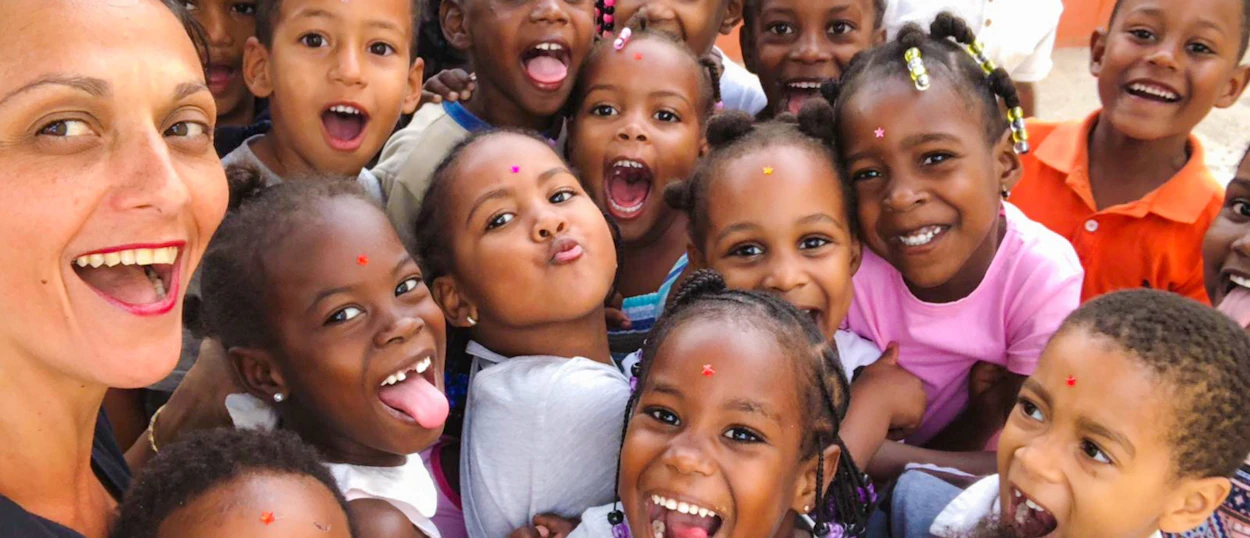 A large group of joyful children and an adult woman smiling and making playful faces.