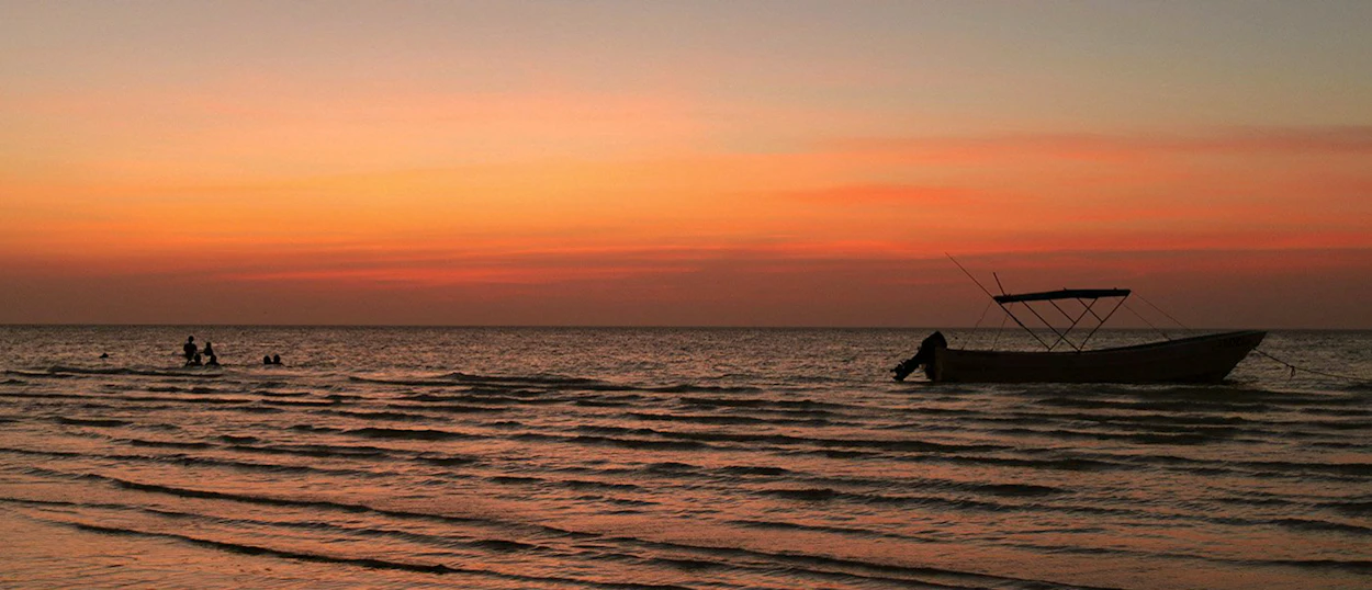 People swim and a boat floats on the calm ocean at sunset in Playa del Carmen.