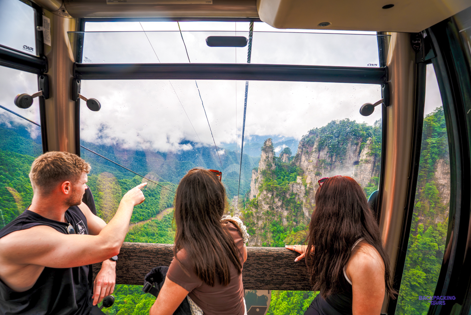 Travellers in a cable car point out at forested sandstone peaks rising from the valley.