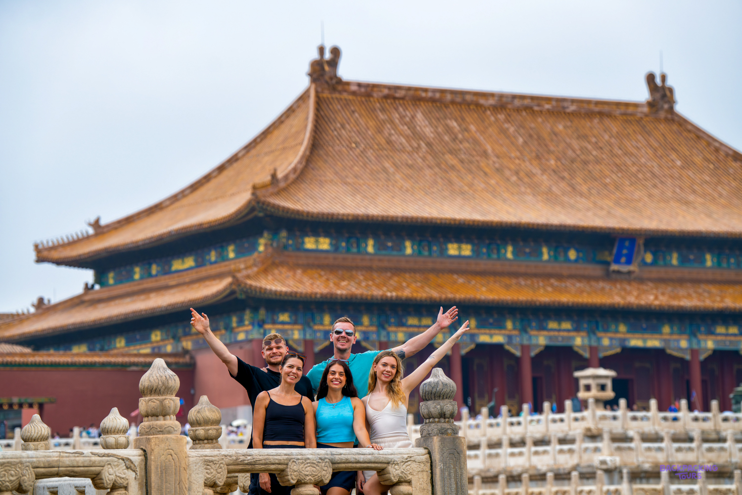 A group of travellers waves and cheers on a marble terrace in front of a golden-roofed palace hall.