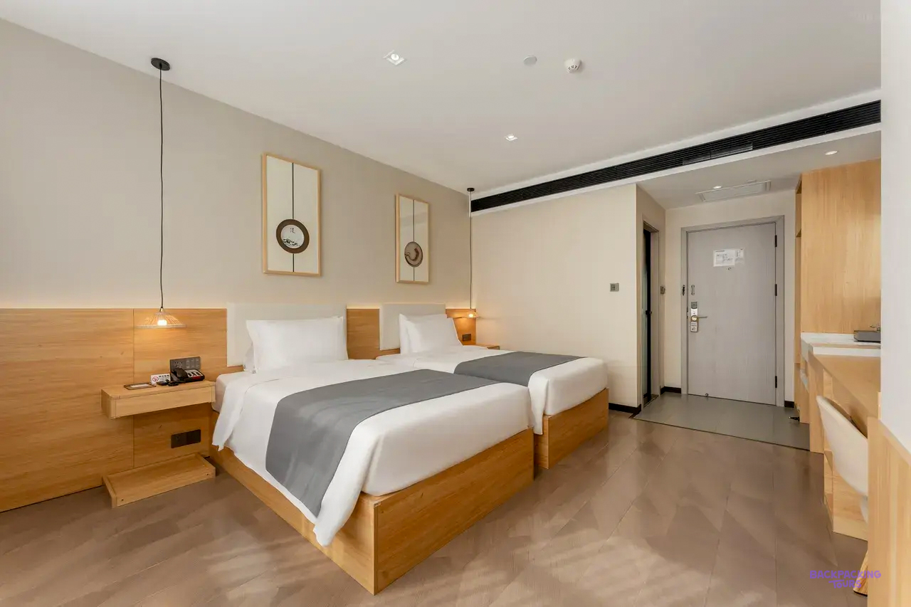 A modern twin room with two single beds, grey runners and light wooden furniture.