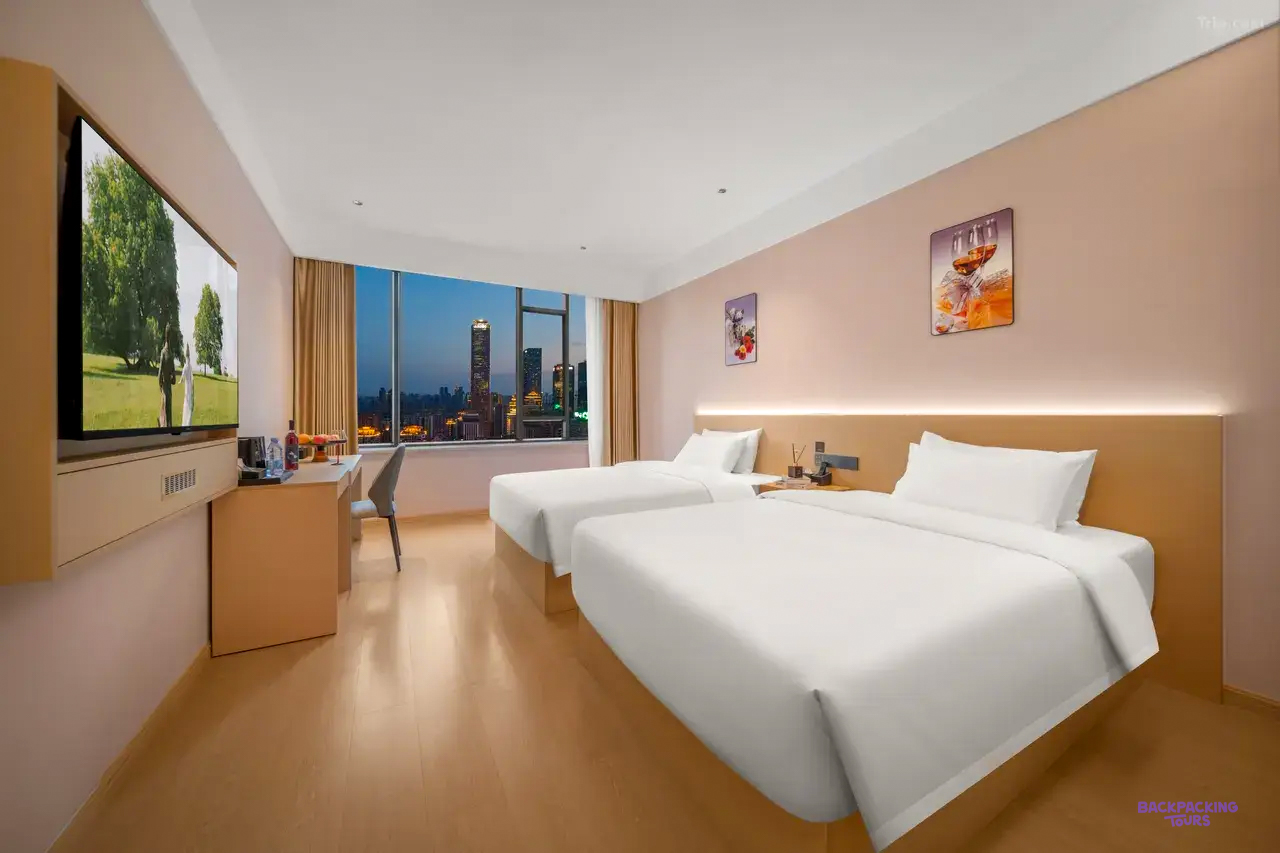A twin room with two white beds and a floor-to-ceiling window looking out over city towers.