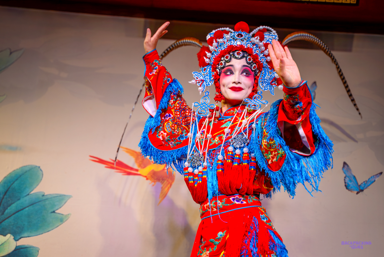 A Sichuan Opera performer in a painted mask and red embroidered costume strikes a pose on stage.