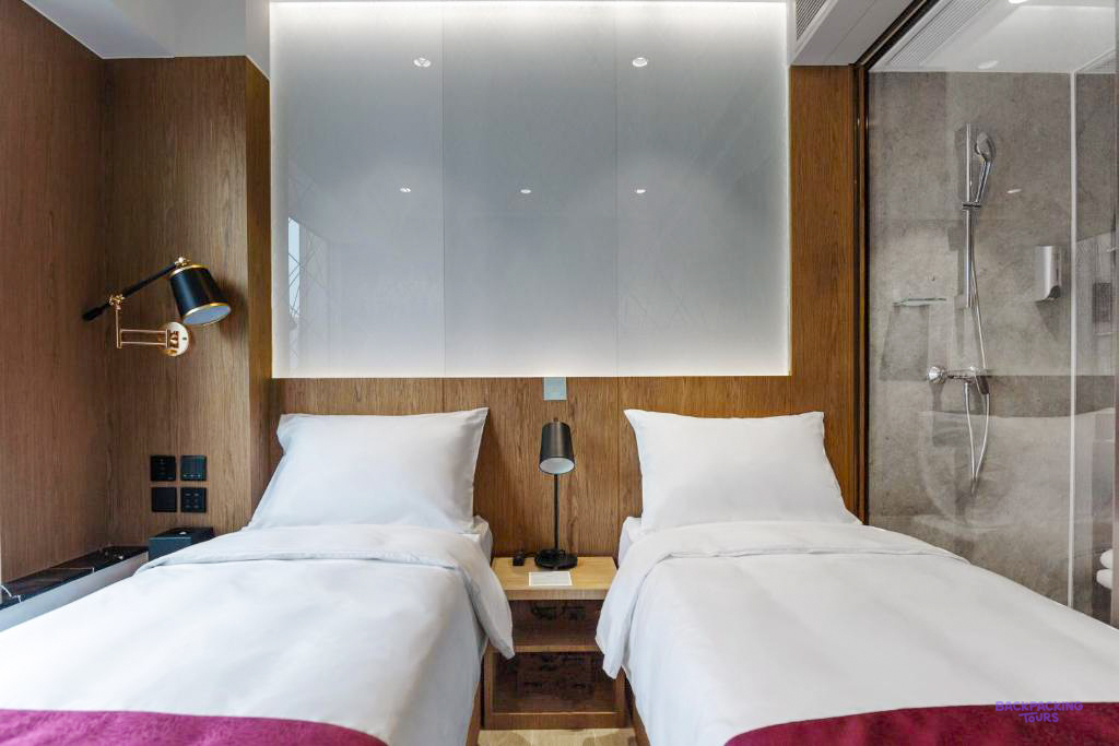 Two single beds with white linen against a wood-panelled wall, beside a glass shower.